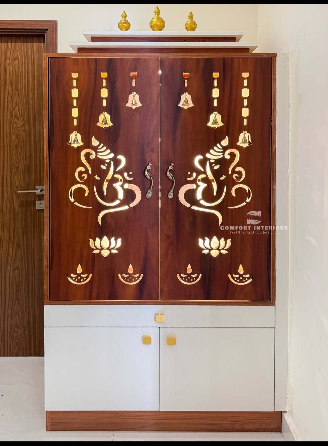 Free-standing pooja unit with backlit laser-cut Ganesha and lotus motifs on rosewood-finish doors, gold finials on top and a white storage cabinet below.