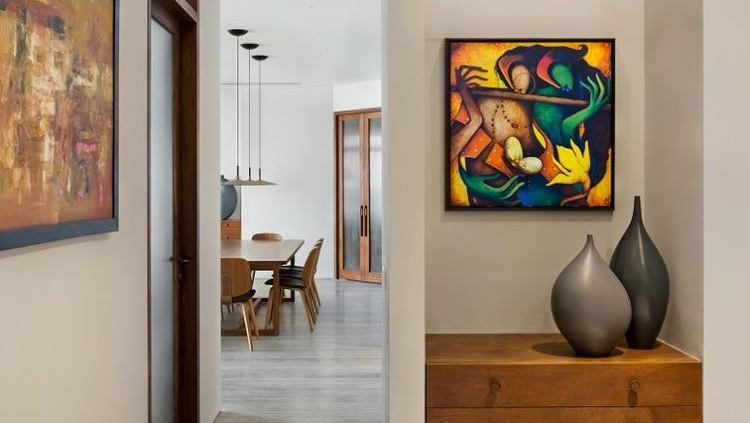 View from a gallery-wall passage, past a wood console with ceramic vases, into a dining area with a wood table, chairs, and a cluster of pendant lights.