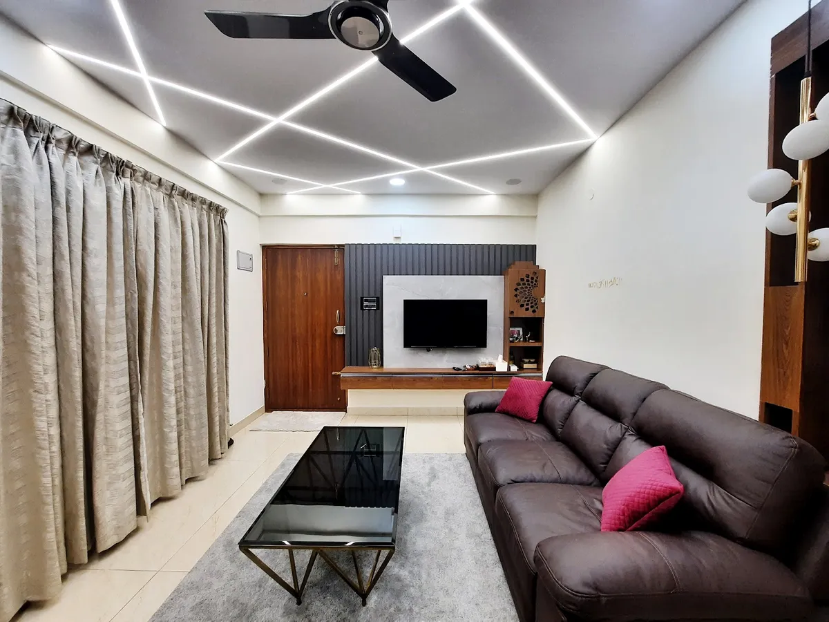 Living room lit by criss-crossing linear profile strips in the ceiling, with a brown leather three-seater carrying magenta cushions