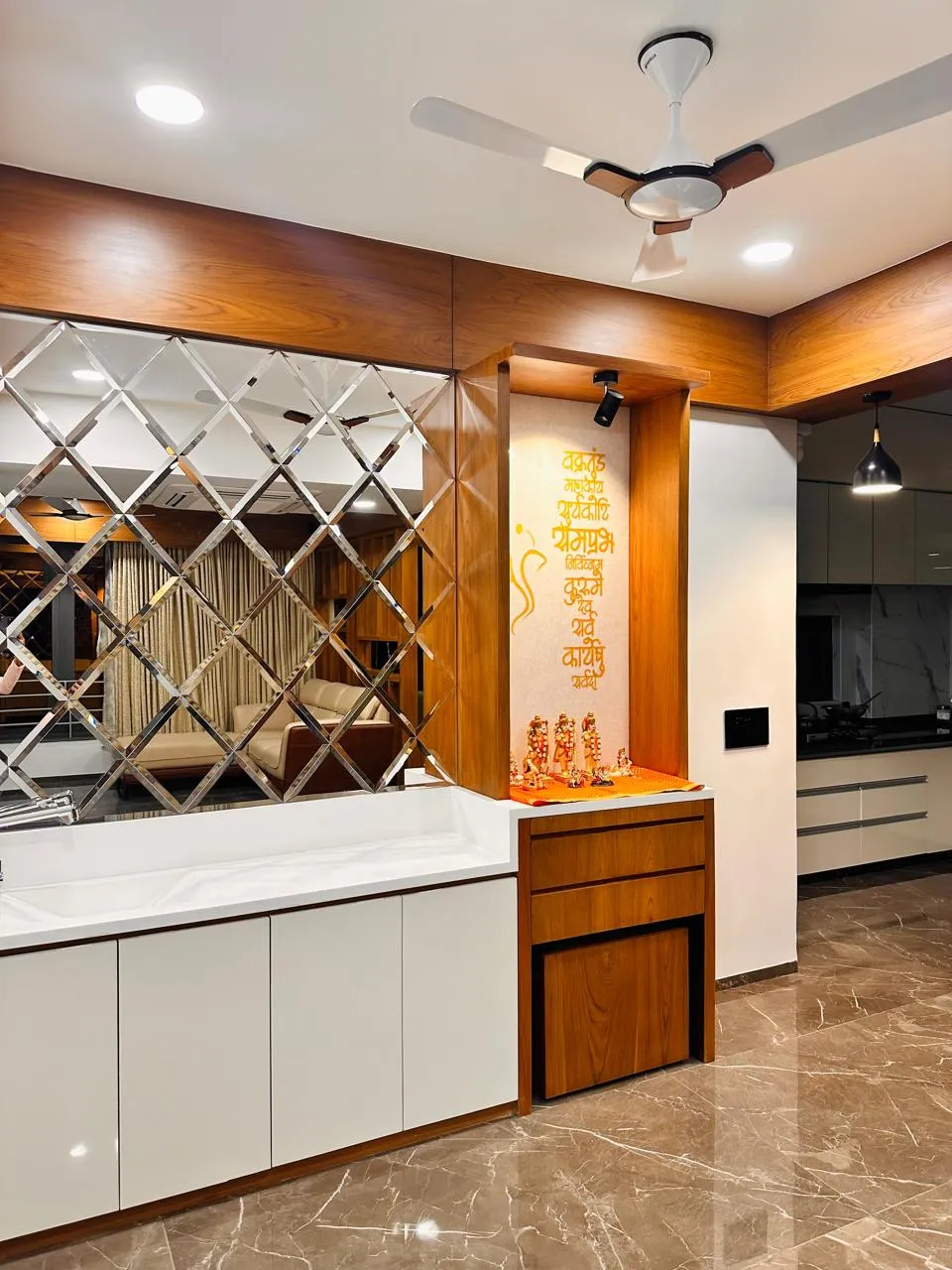 Teak-framed pooja niche with a saffron Ganesh shloka on the back wall and brass idols on an orange platform