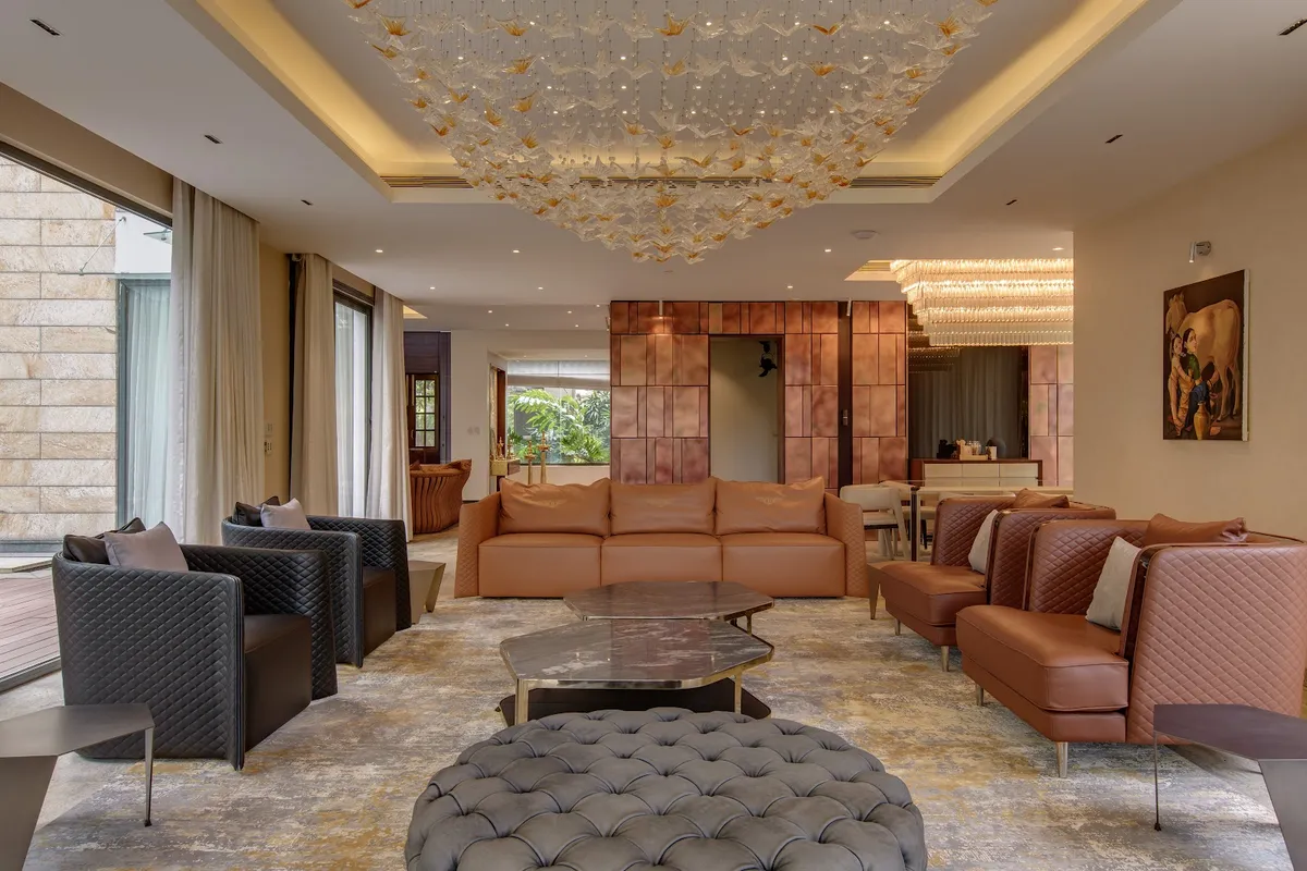 Large villa living room with tan leather sofas and quilted charcoal armchairs around a grey buttoned ottoman and stacked stone tables