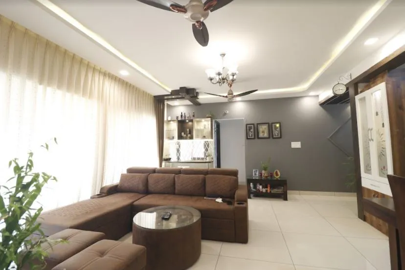 Brown fabric L-sofa with pull-out headrests and a round glass coffee table in front of a charcoal-grey accent wall hung with three small frames