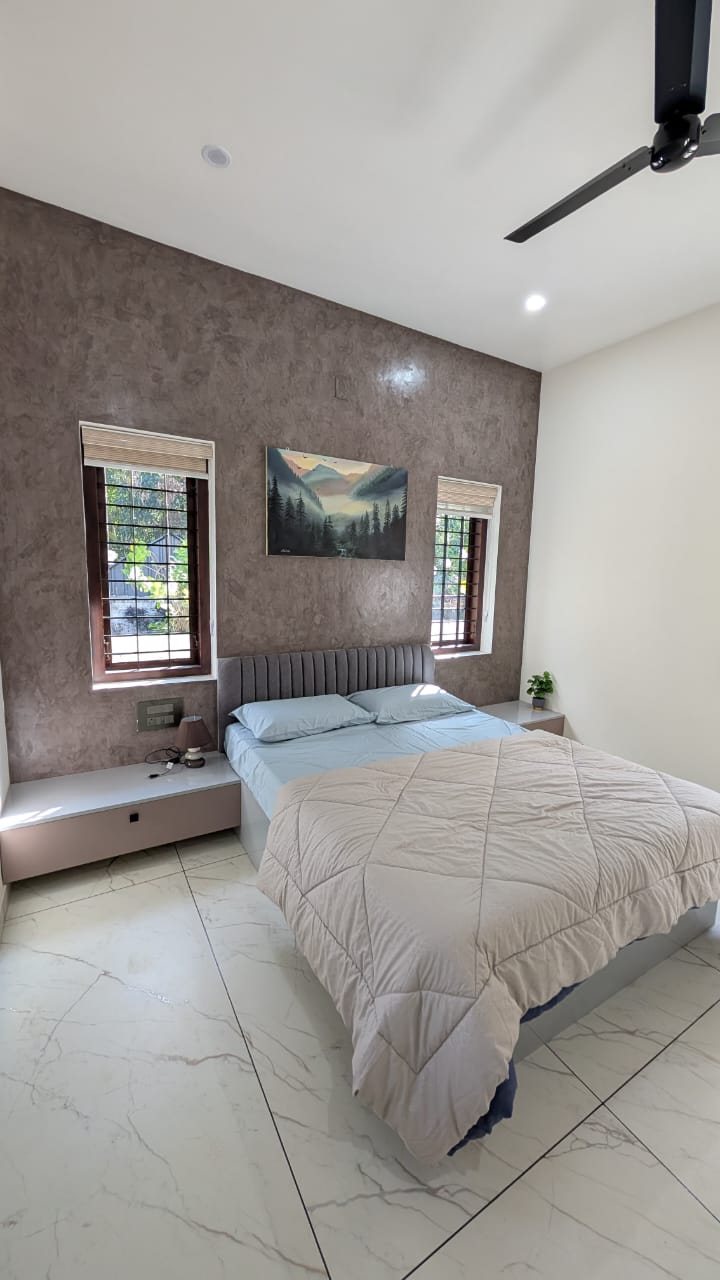 Bedroom with a mauve textured accent wall, a channel-tufted grey upholstered headboard, and floating two-tone nightstands flanking wood-framed windows.
