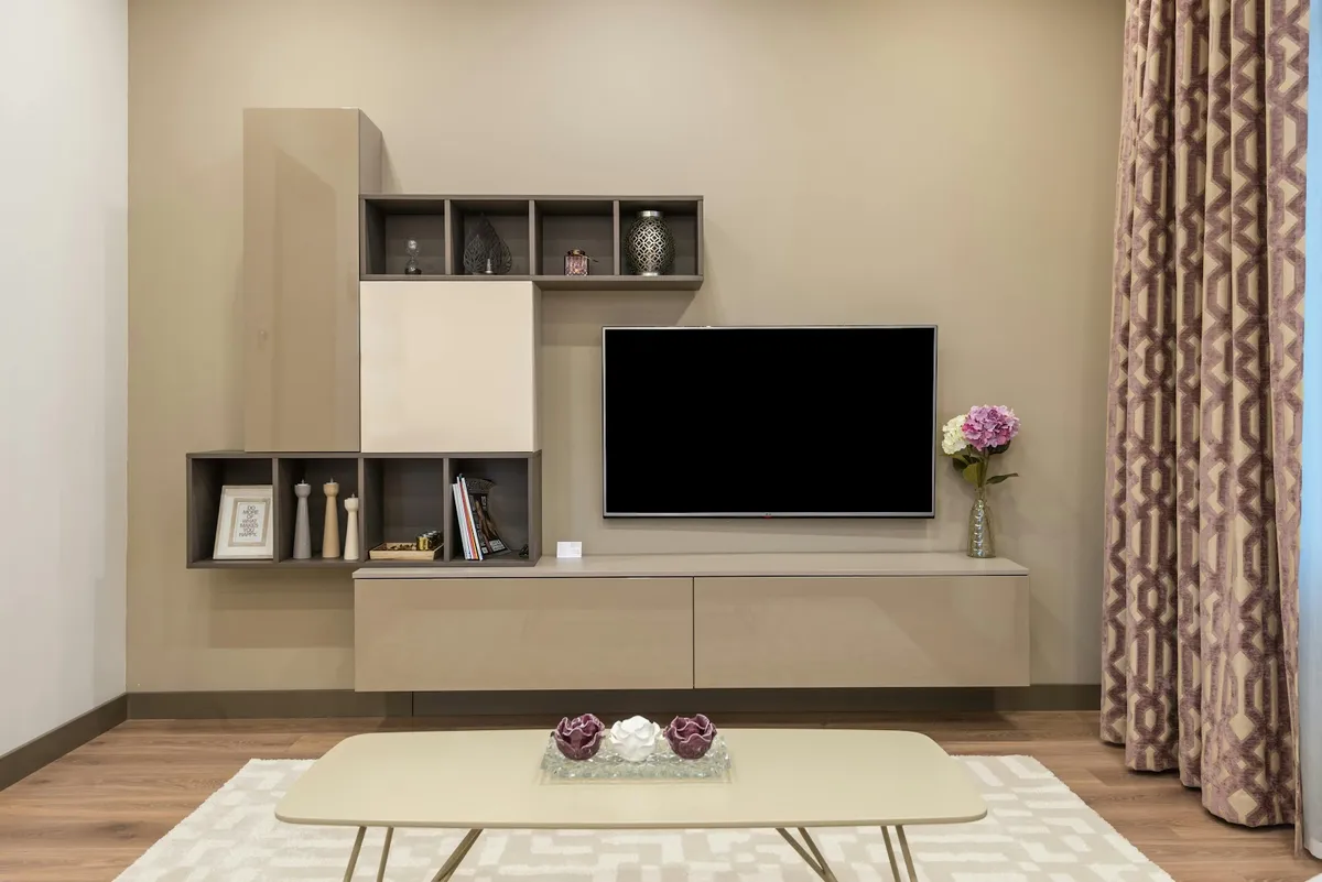 Living room TV wall with a taupe modular cabinet featuring open cubby shelving styled with decor accessories, patterned drapes