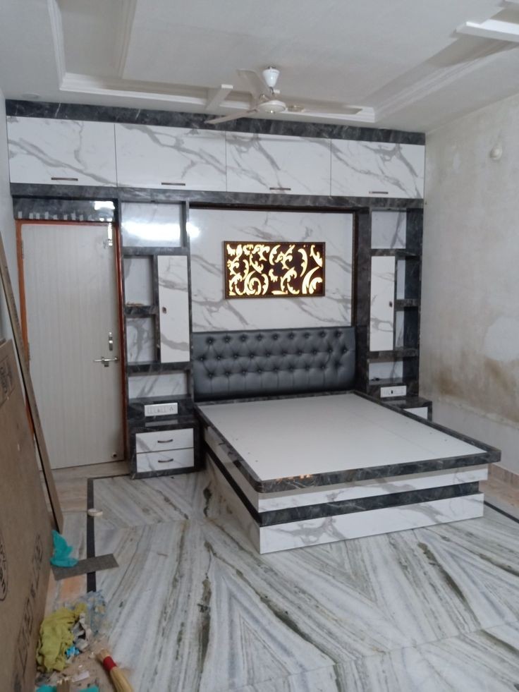 Marble-finish laminate platform bed with a backlit floral jaali headboard panel and matching overhead loft units, under a cove-lit false ceiling.