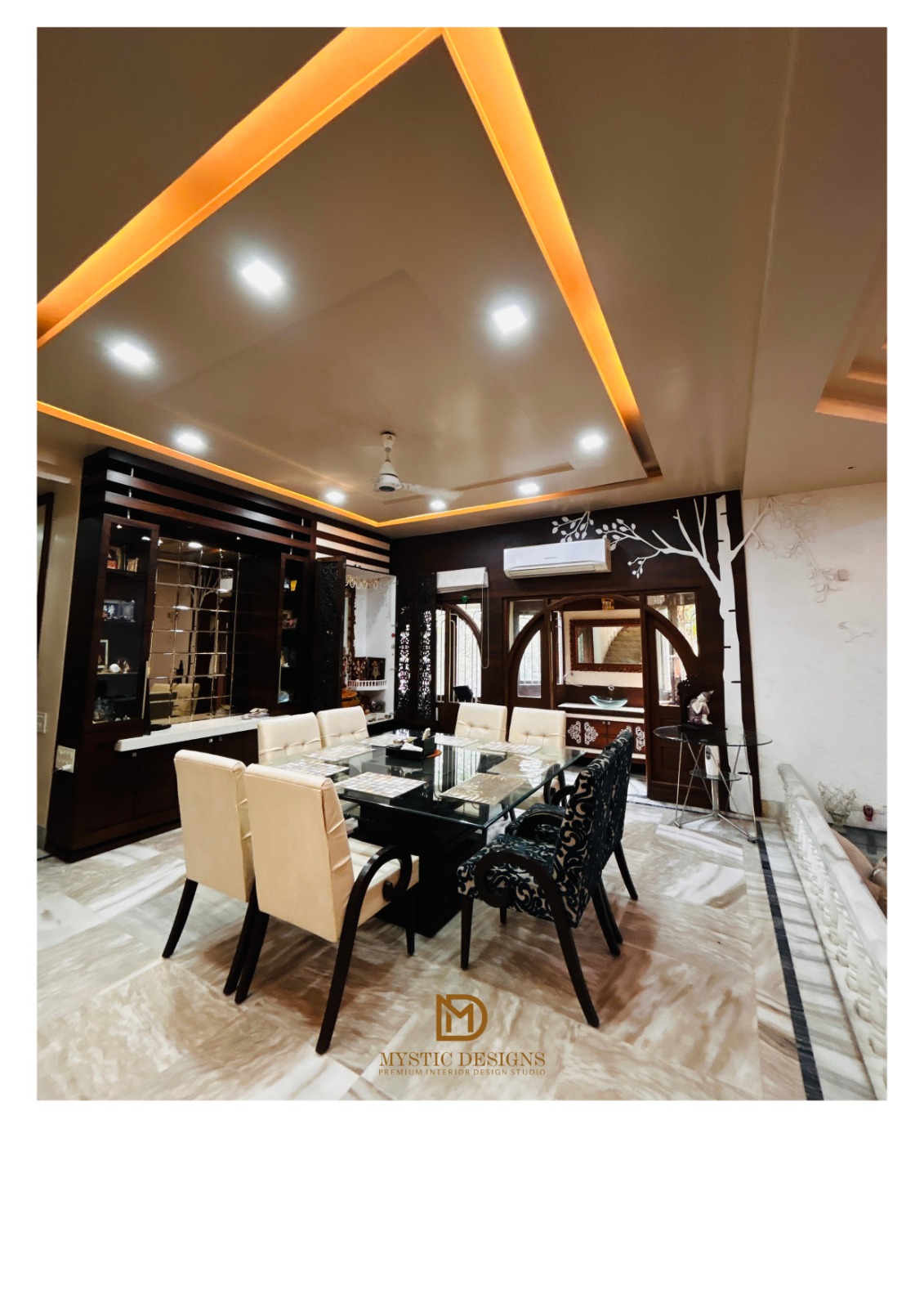 Dining room with a black glass-top table seating eight in cream and patterned upholstered chairs, a dark wood mirrored display cabinet