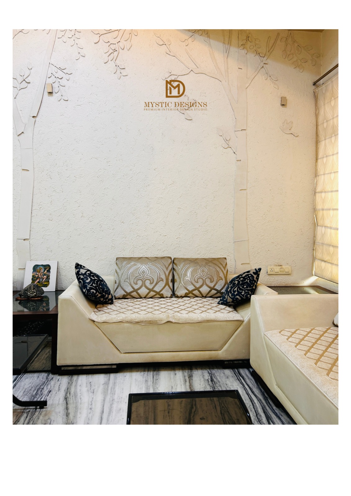 A living room with a 3D textured stucco tree-branch feature wall behind a cream tufted sofa set with gold-patterned and navy accent cushions, on marble flooring