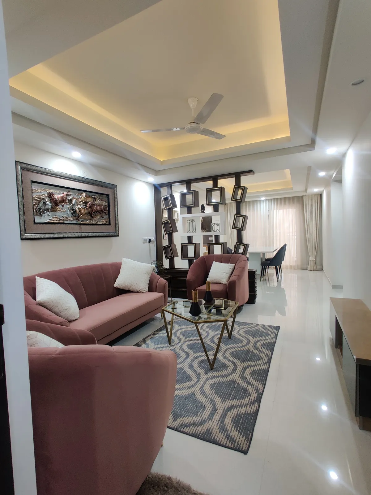 Living room of an Indian flat with a dusty-rose channel-tufted sofa set around a gold hexagonal glass table on an indigo wave-pattern rug