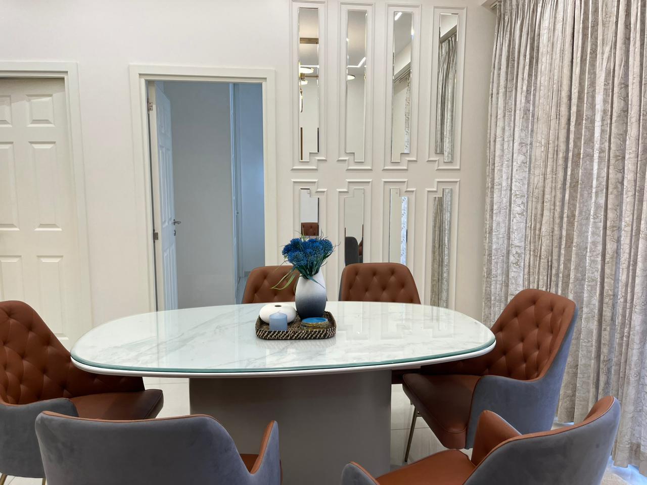 Dining room with an oval marble-top table, tufted brown and grey chairs, a mirrored geometric panel wall, and floor-to-ceiling textured curtains.