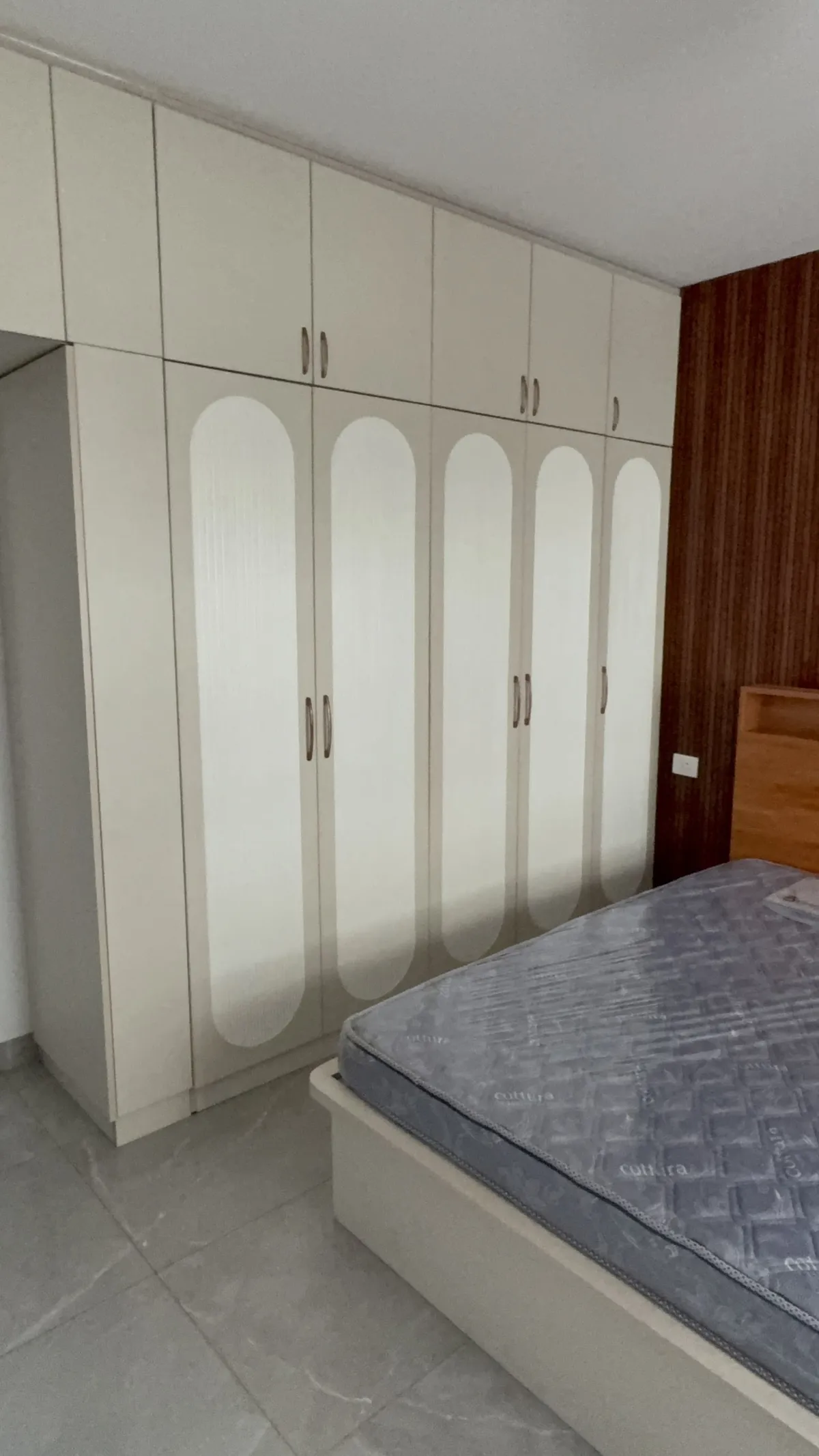 Bedroom at handover stage: a full-height cream wardrobe run whose five shutters each carry a tall arched fluted inlay