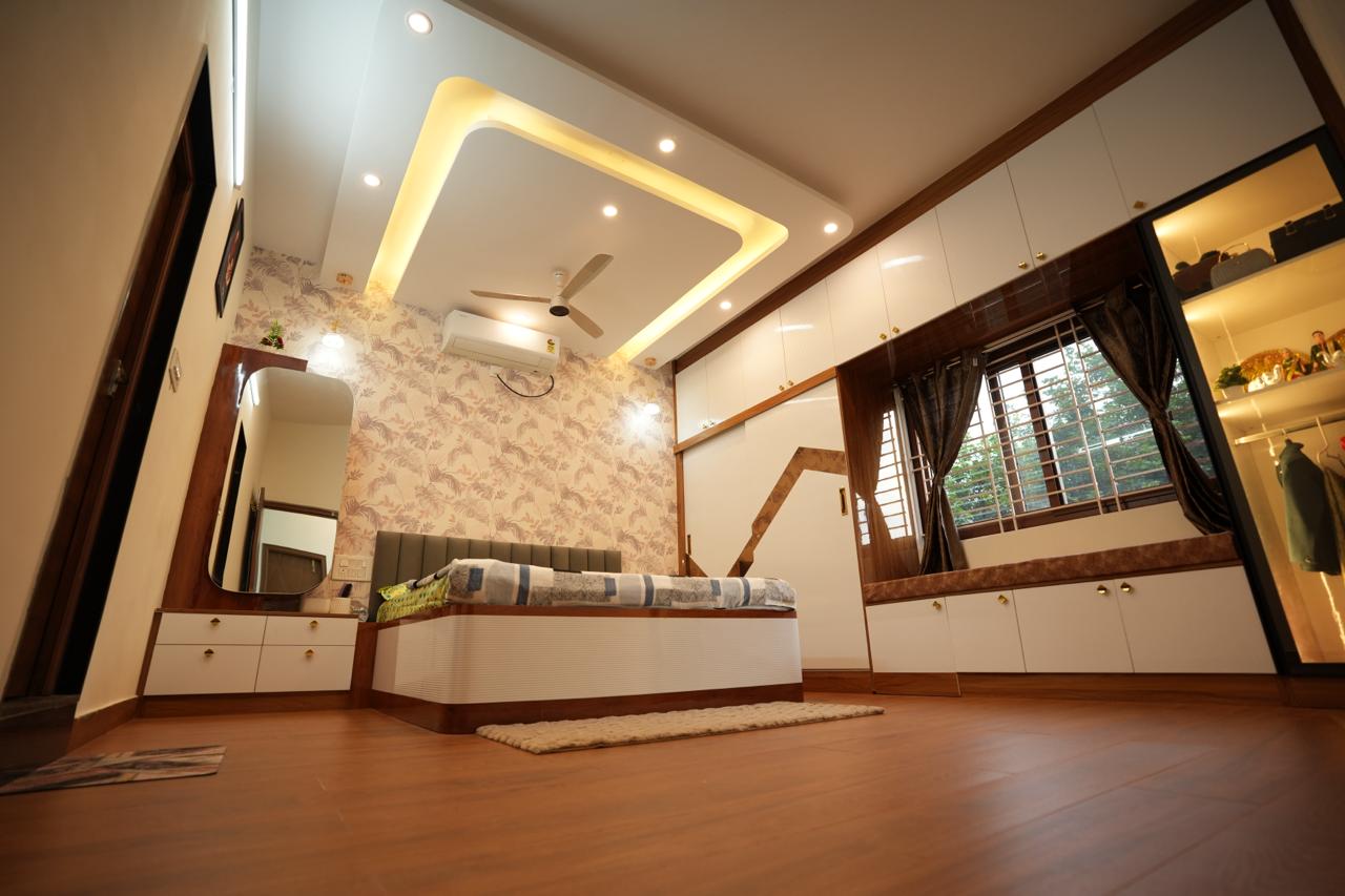 Master bedroom with a floral wallpaper accent wall, a backlit square cove ceiling, a wood dressing unit with mirror, and a window-seat storage bench.