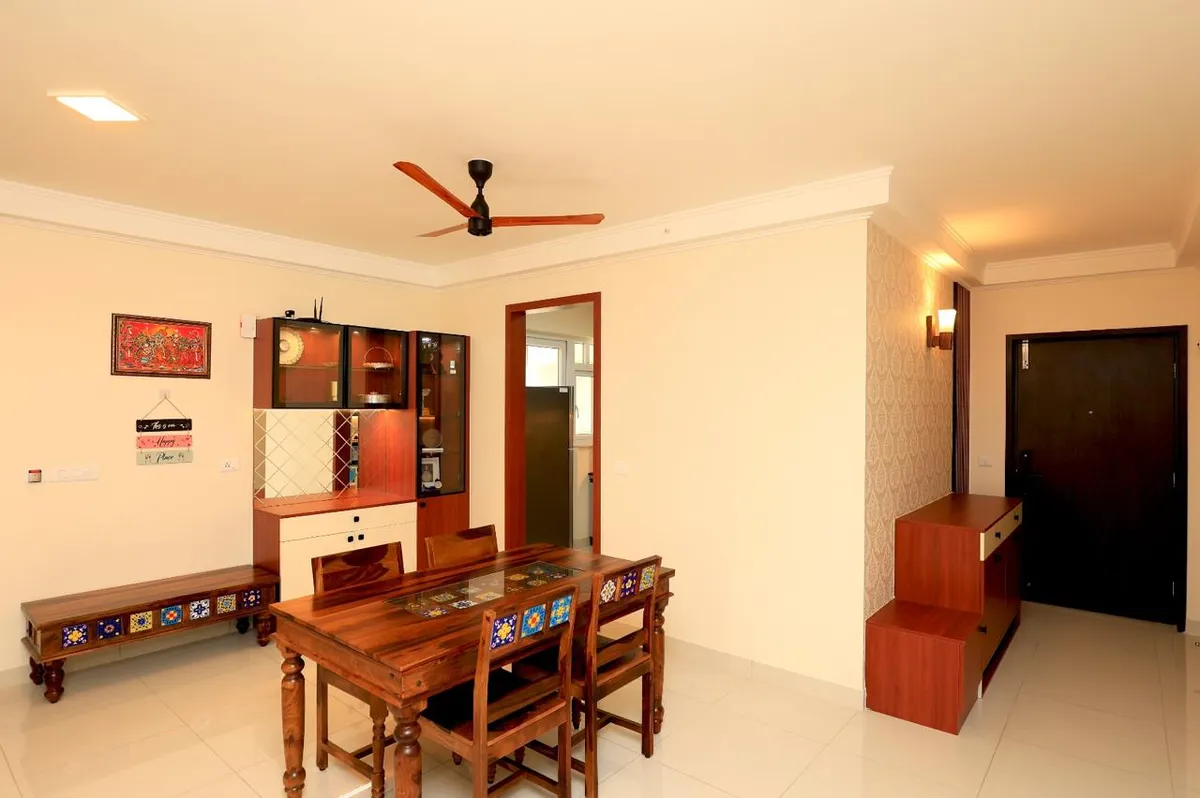 Dining corner of an Indian flat with a sheesham six-seater and a matching low bench, both inlaid with blue-and-yellow ceramic tiles