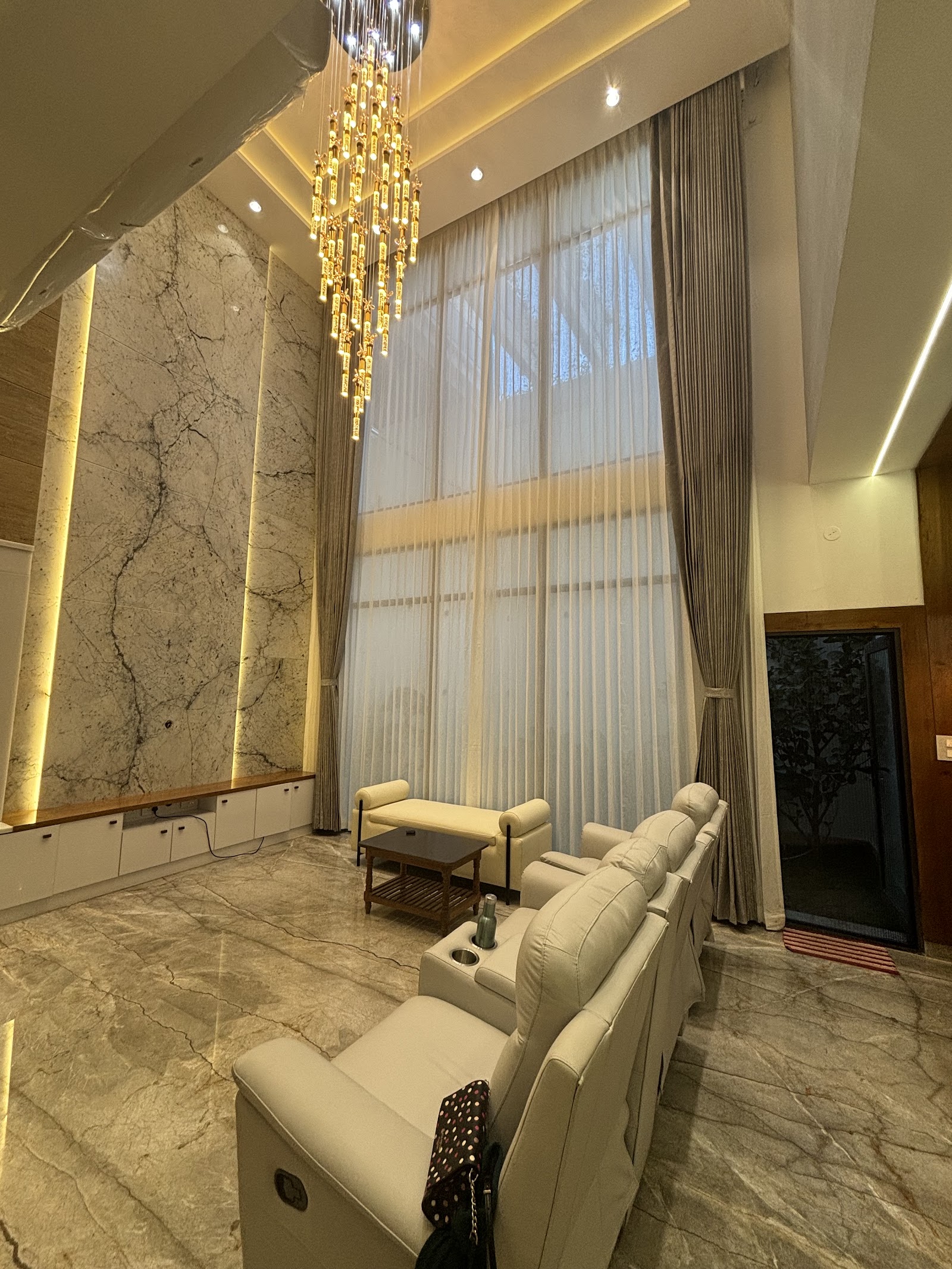 Double-height living room with a book-matched marble feature wall, a spiral crystal-drop chandelier, floor-to-ceiling sheer and blackout curtains