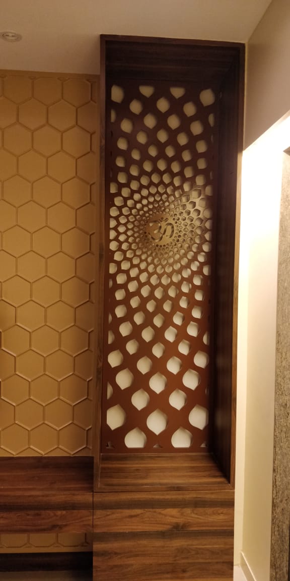 Close-up of a wood-framed pooja niche with a laser-cut jaali screen featuring a radiating dot pattern and a central Om symbol
