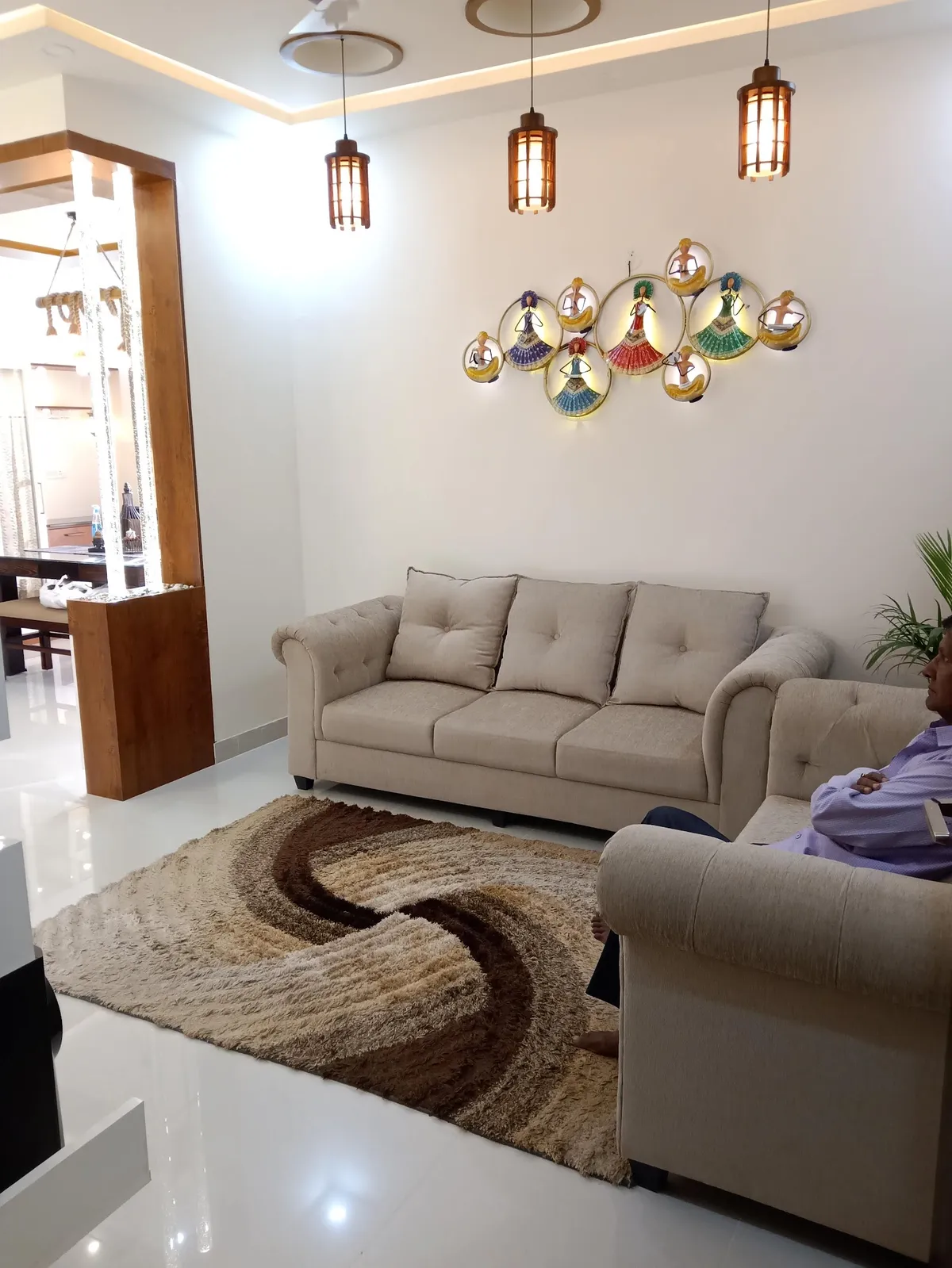 Living room with beige tufted chesterfield-style sofas, three cage-style pendant lights, an illuminated dancer-figurine wall art piece