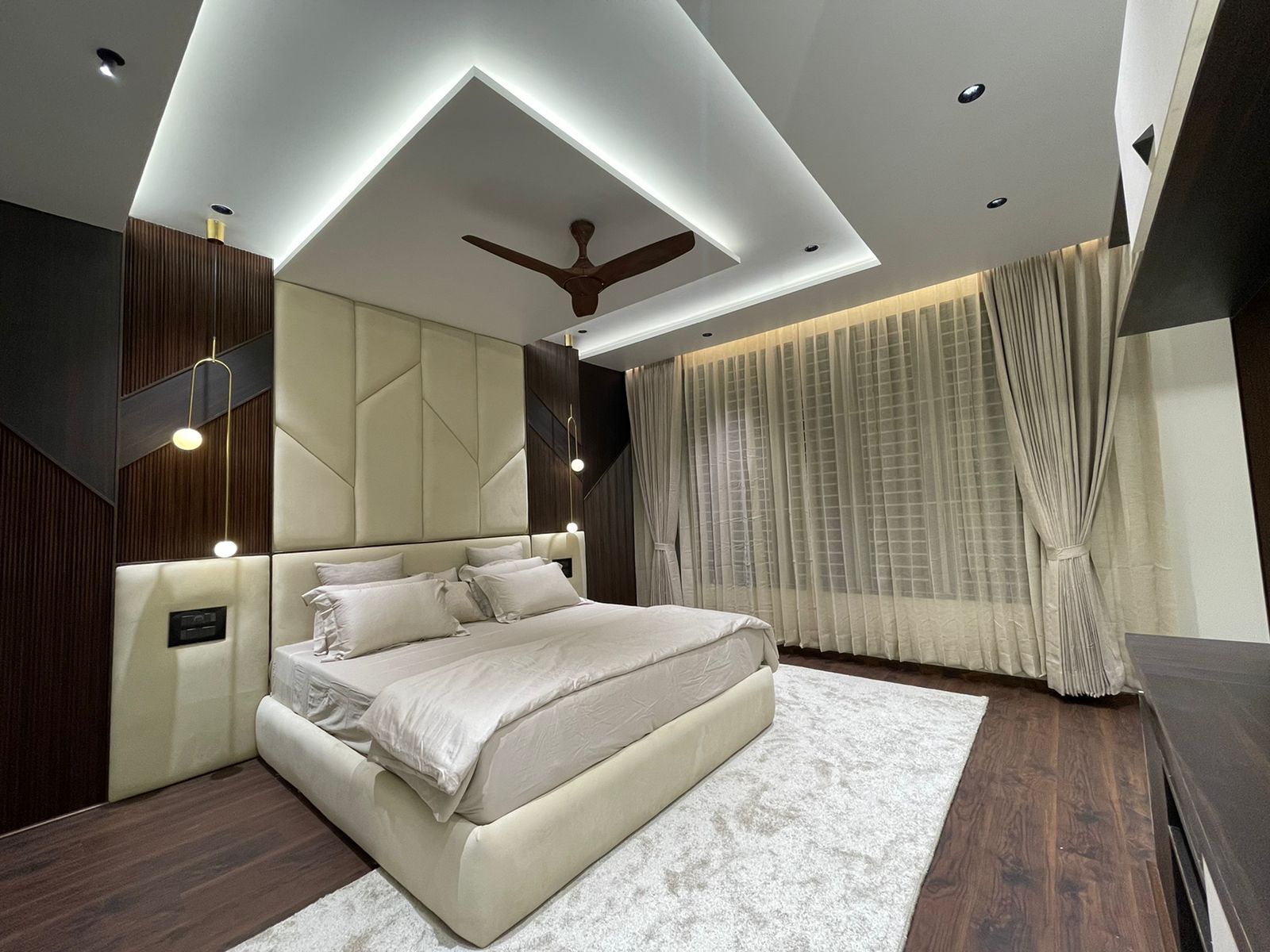 Master bedroom with a geometric channel-tufted cream headboard wall that extends up into an angular cove-lit false ceiling