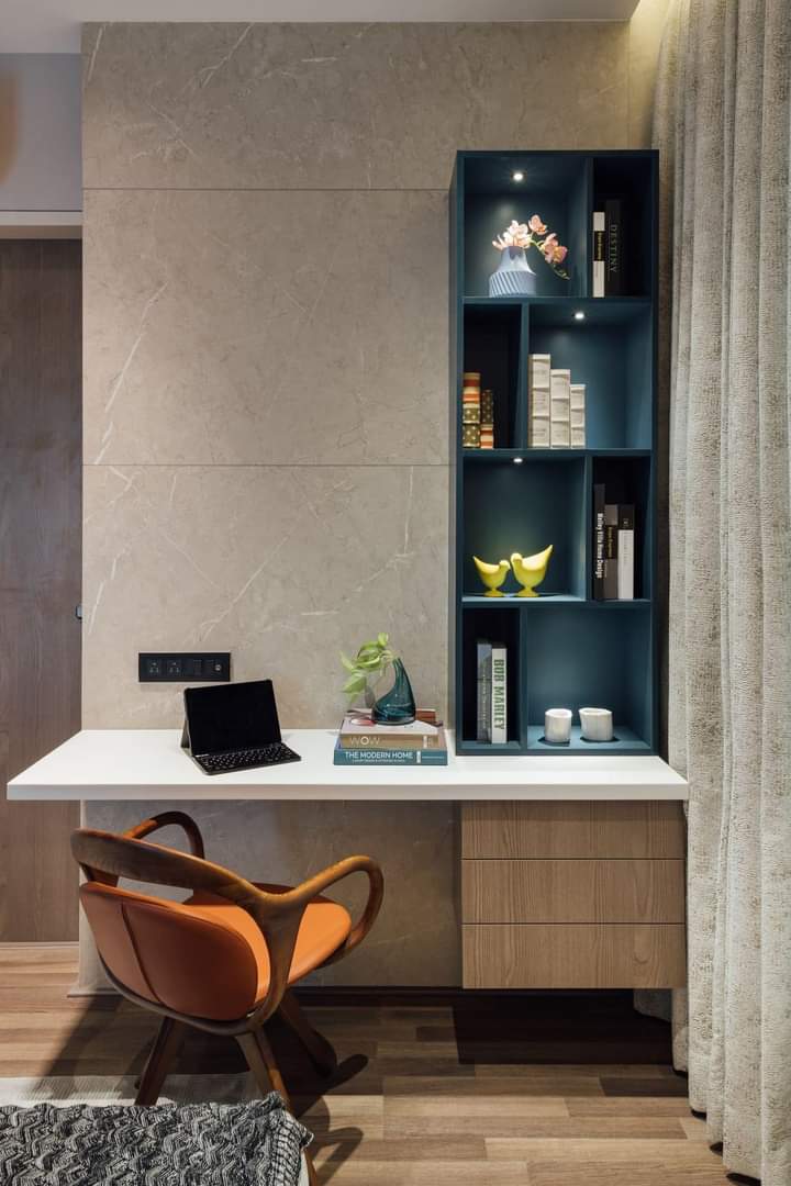 Study nook with a floating white desk against a marble-clad wall, a teal built-in bookshelf with lit display niches, and a curved wood-frame leather chair.