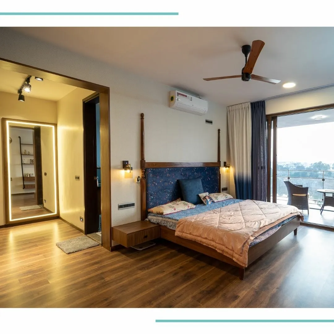 Real photo of a master bedroom with a four-poster wood bed with a blue upholstered headboard, a mirrored dressing alcove to the side
