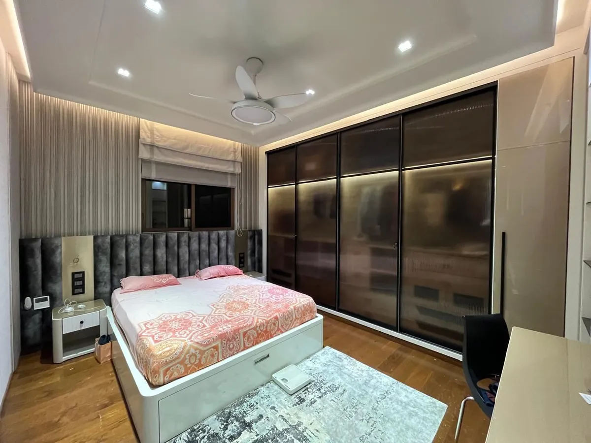 Lived-in bedroom with a grey channel-tufted headboard wall running behind the bed into two bedside units, a full-width sliding wardrobe in bronze-tinted glass