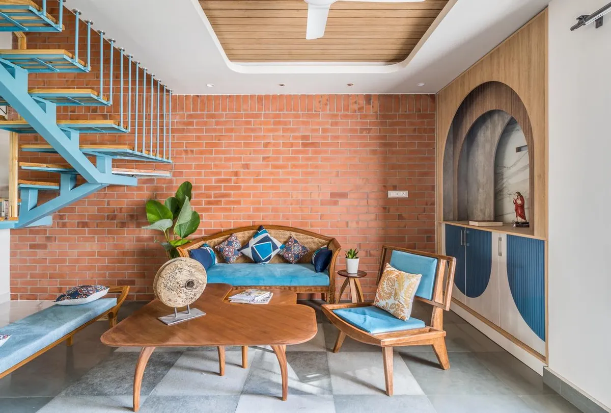 Living room with an exposed brick feature wall, a blue spiral staircase, a cane-back sofa in teal velvet, and a checkerboard-tile floor.