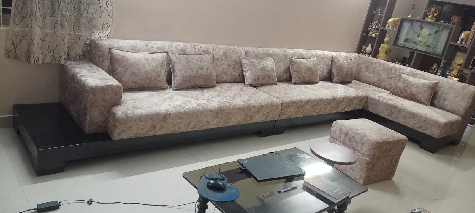 Living room with an L-shaped floral-upholstered sectional sofa and matching ottoman around a glass coffee table cluttered with a laptop and papers