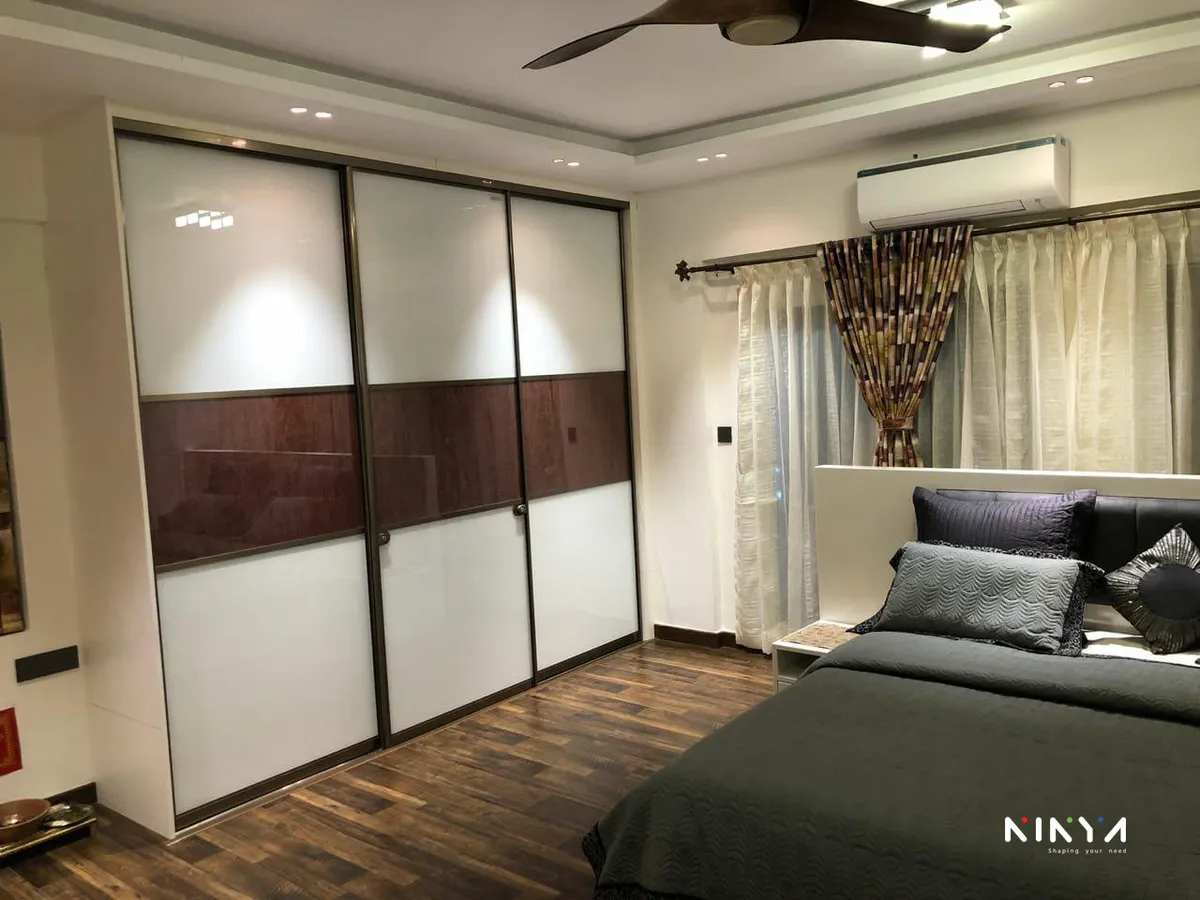 Bedroom where a three-shutter sliding wardrobe in white back-painted glass, banded across the middle in dark walnut