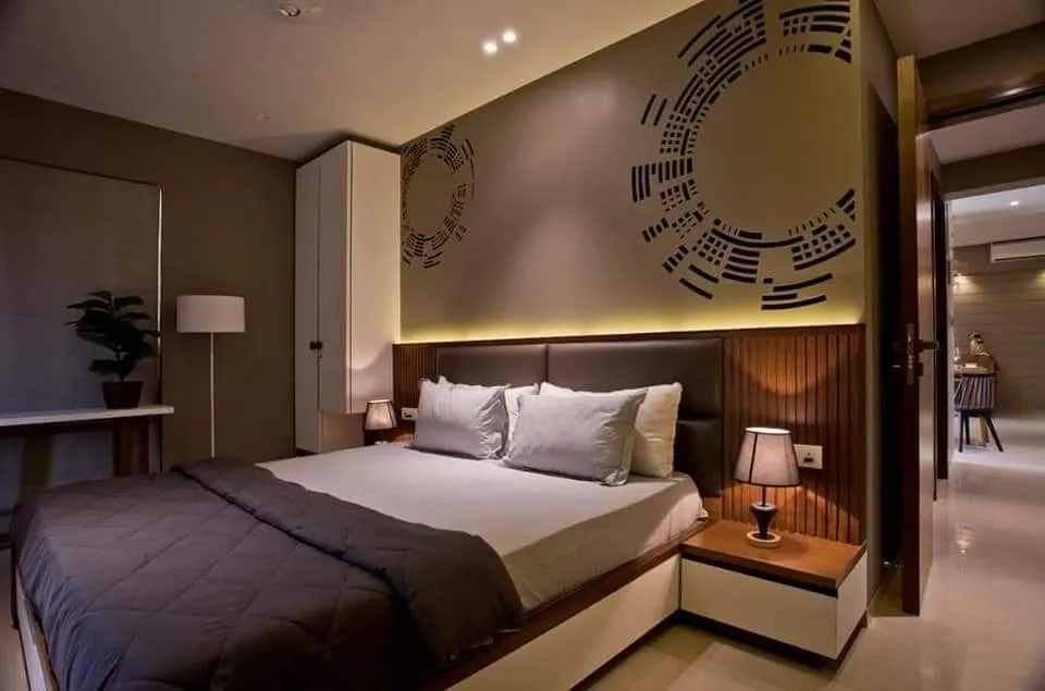 Bedroom with a fluted wood headboard panel lit by a concealed strip, a dark upholstered headboard between wall-hung white bedside drawers