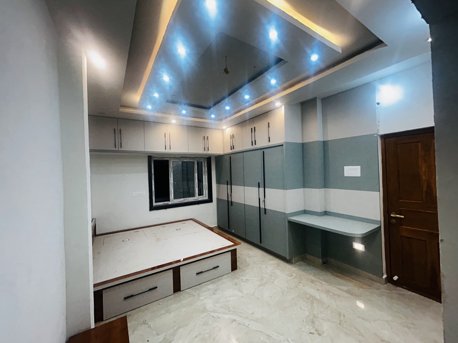 Bedroom under fit-out with a multi-tier POP ceiling with blue accent lighting, a two-tone grey wardrobe wall