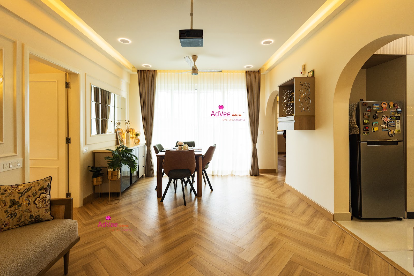 Dining area with a herringbone-pattern wood floor, a four-seat dining table, and an arched opening to the kitchen with a small wall-mounted display niche.
