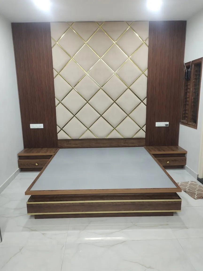 A bedroom with a diamond-tufted cream and gold headboard wall flanked by fluted wood panelling, and a wood platform bed with floating nightstands