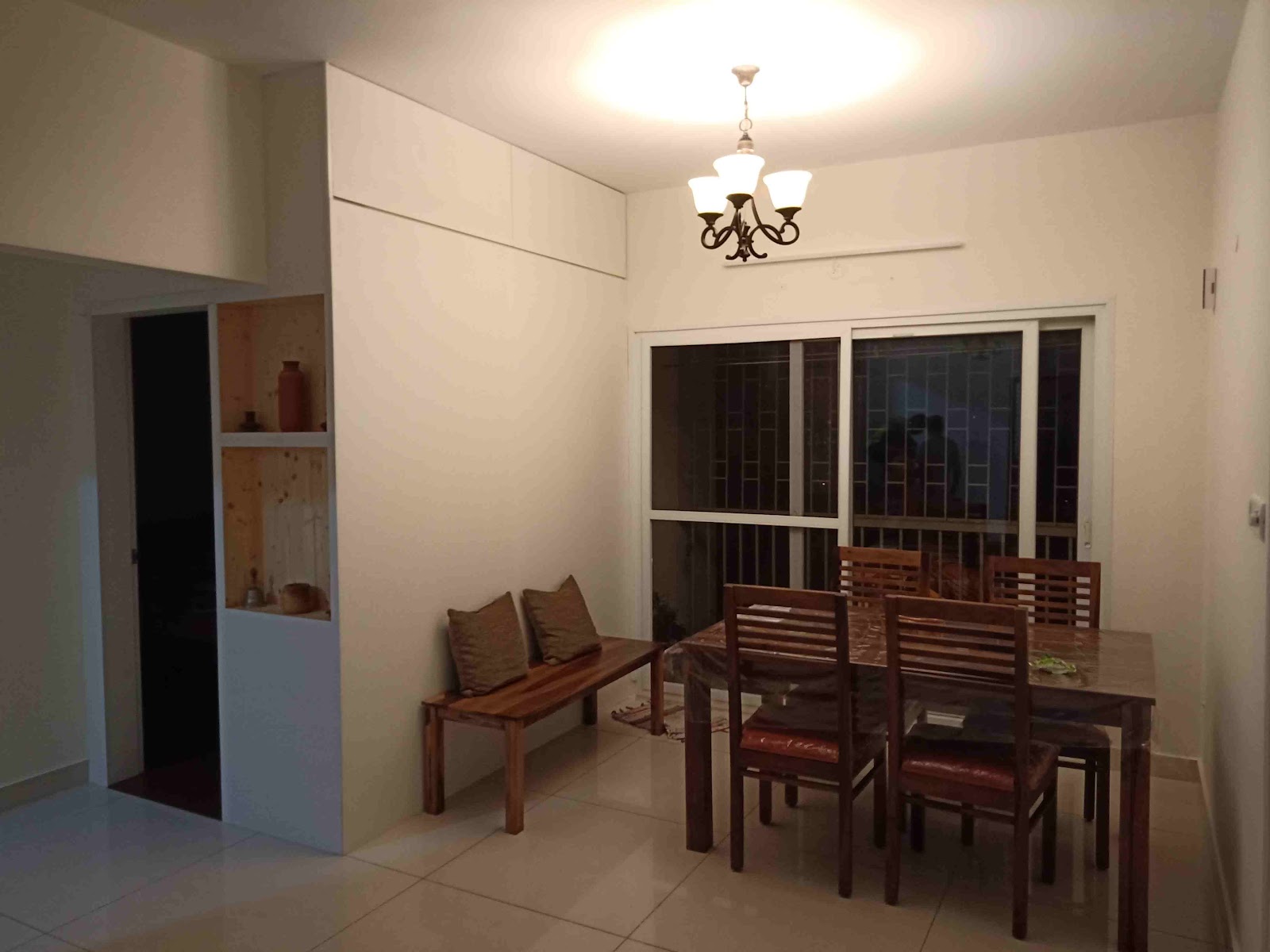 Dining nook with a sheesham wood table and chairs still wrapped in packaging plastic, a cushioned bench along the wall