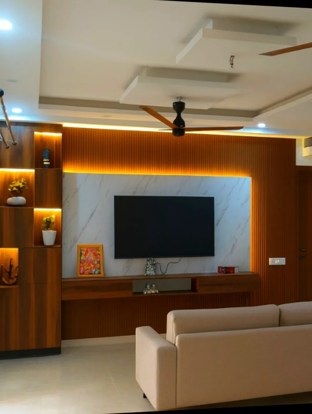 Living room TV feature wall with a backlit white marble panel framed by warm wood fluted panelling, layered pop ceiling with cove lighting