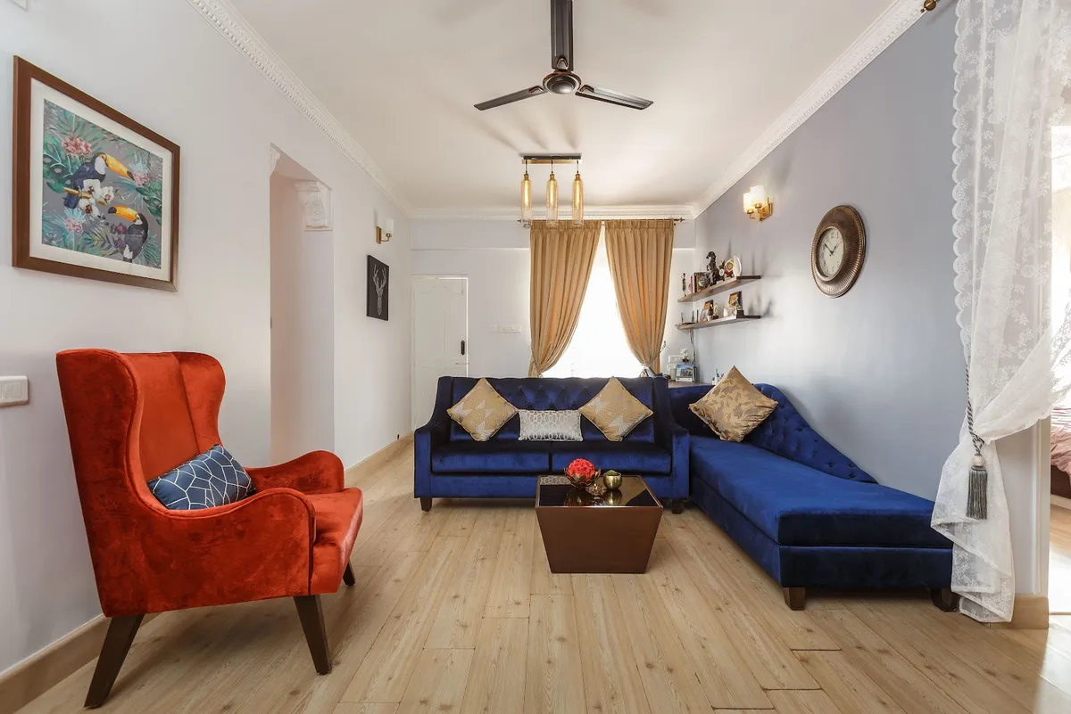 Living room with a navy velvet L-shaped tufted sofa, a rust-orange wingback armchair, a three-bulb Edison pendant cluster overhead