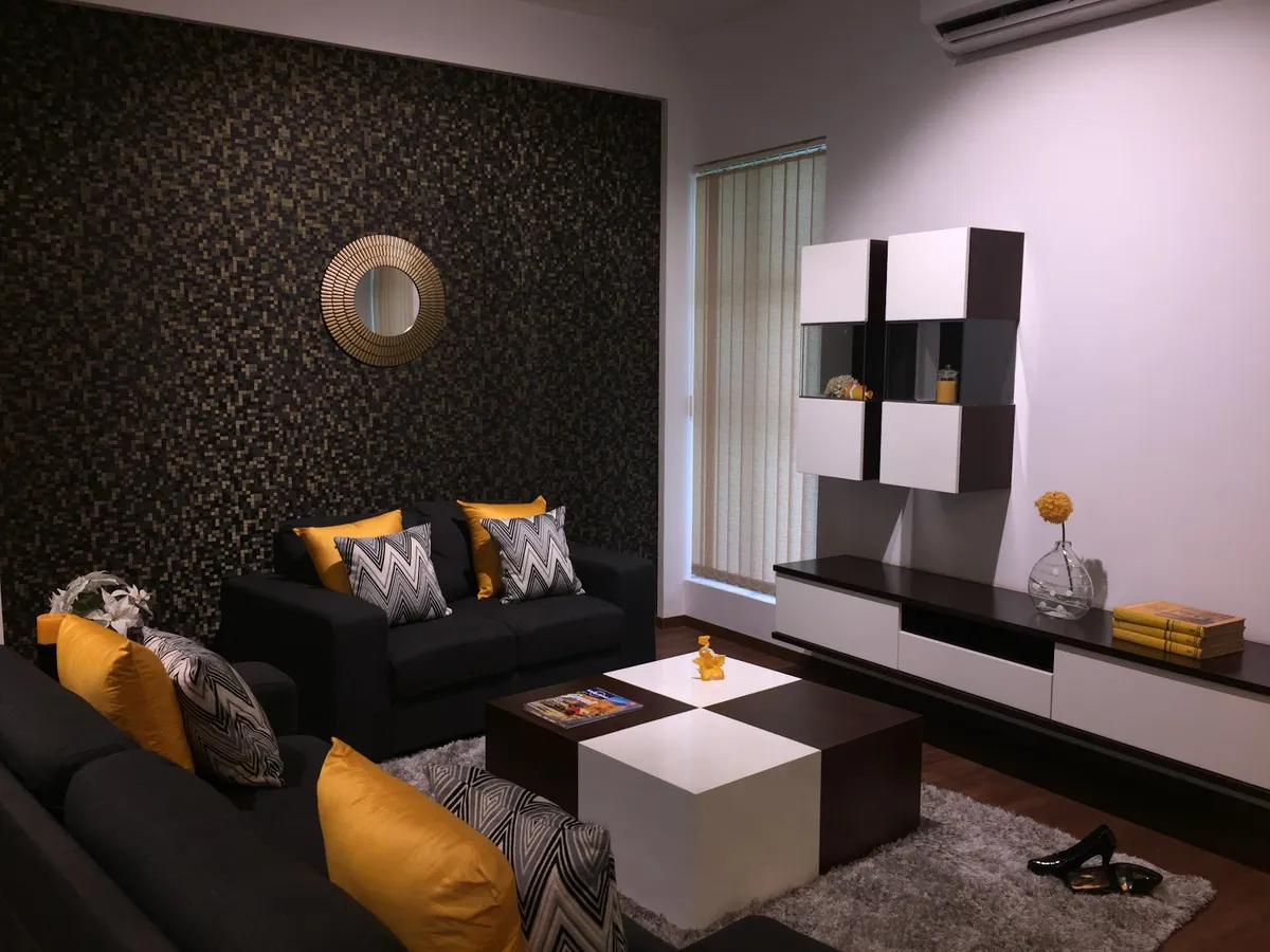 Living room with a dark mosaic-tile feature wall and a sunburst mirror, charcoal sofas dressed in mustard and chevron cushions