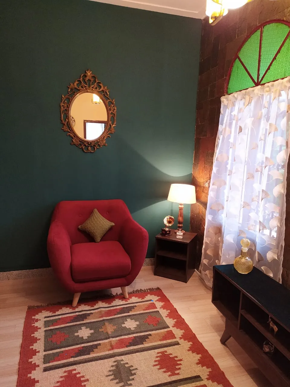 Corner seating vignette with a crimson tub chair on a kilim dhurrie against a bottle-green wall