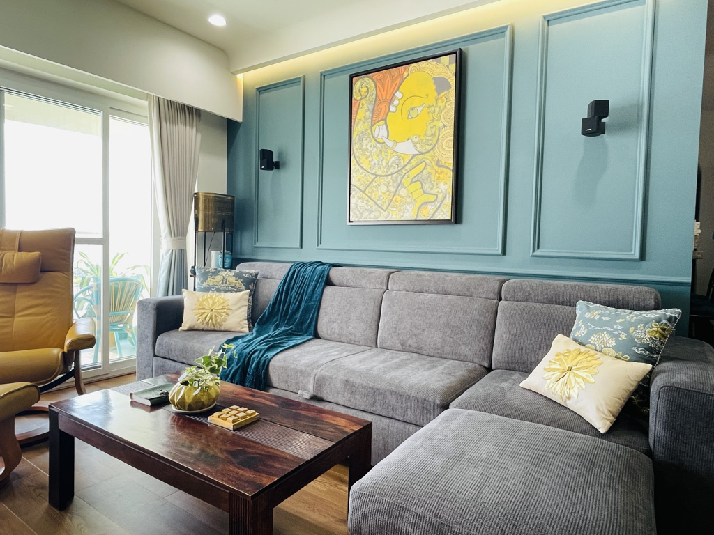 Living room with teal moulded wall panelling and a framed abstract art print behind a grey corner sectional sofa.