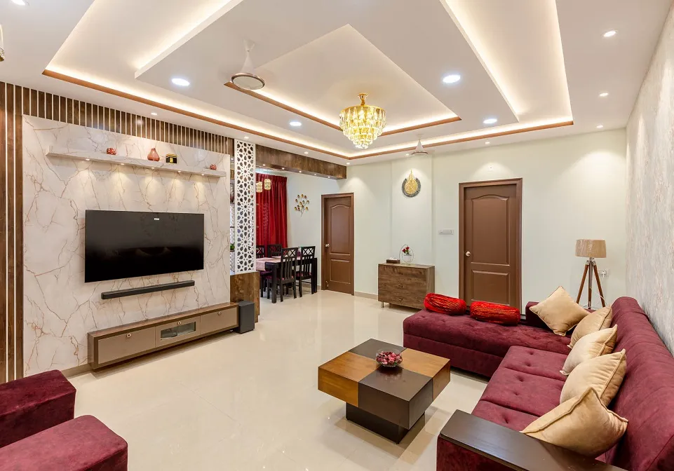 Real photo of a living room with a marble-clad TV wall framed by fluted wood trim, a multi-tier cove-lit pop ceiling with a crystal chandelier