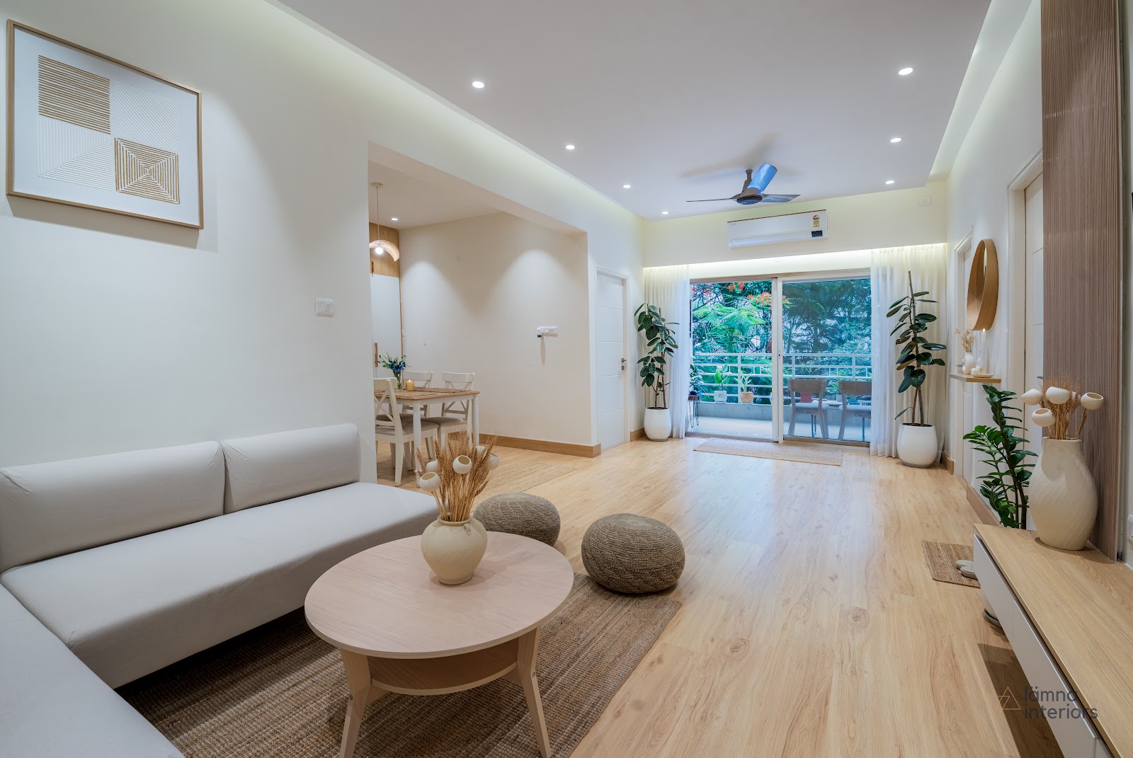 Open-plan living room with a light-grey sofa, round wood coffee table, woven poufs and a jute rug on light wood-plank flooring, opening onto a balcony