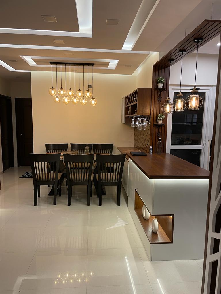 Dining area with a cluster of amber globe pendants over a dark wood dining table, and an adjoining bar counter with wine-glass racking and cage pendant lights.