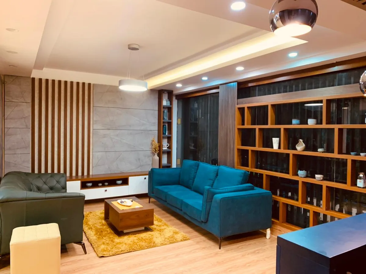 Living room with a peacock-blue velvet sofa facing a dark green tufted leather armchair across a mustard shag rug