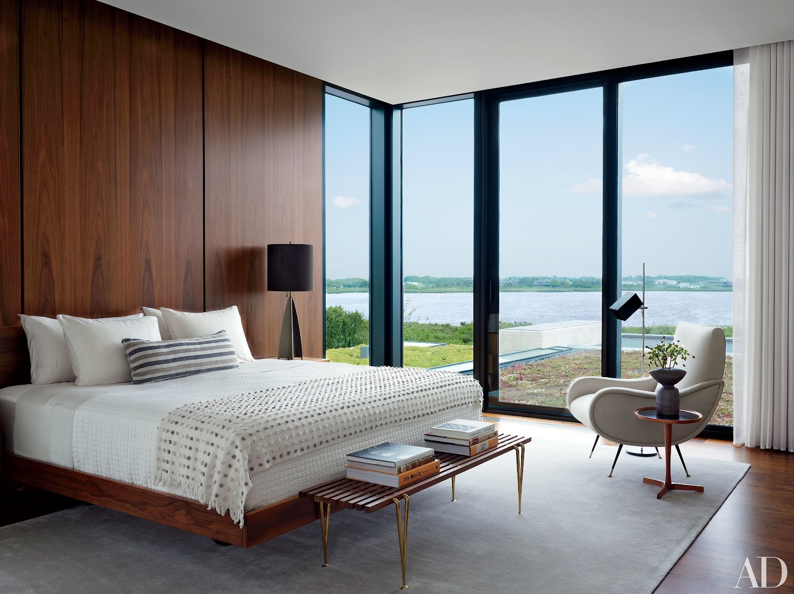 Bedroom with a walnut-panelled wall behind the bed and floor-to-ceiling glazing overlooking a waterfront view