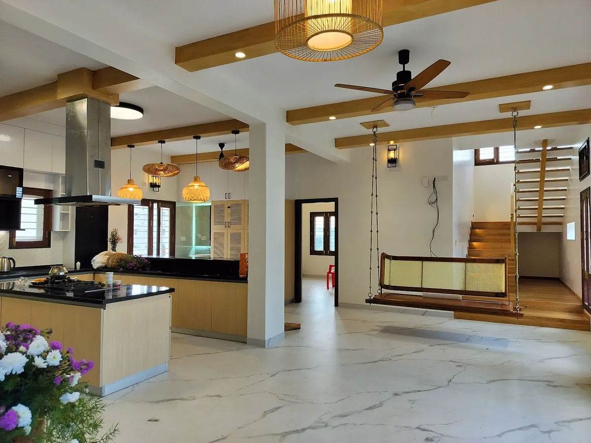 Open-plan hall with a black-granite island kitchen and stainless chimney at one end, woven cane pendants under a wooden beam grid