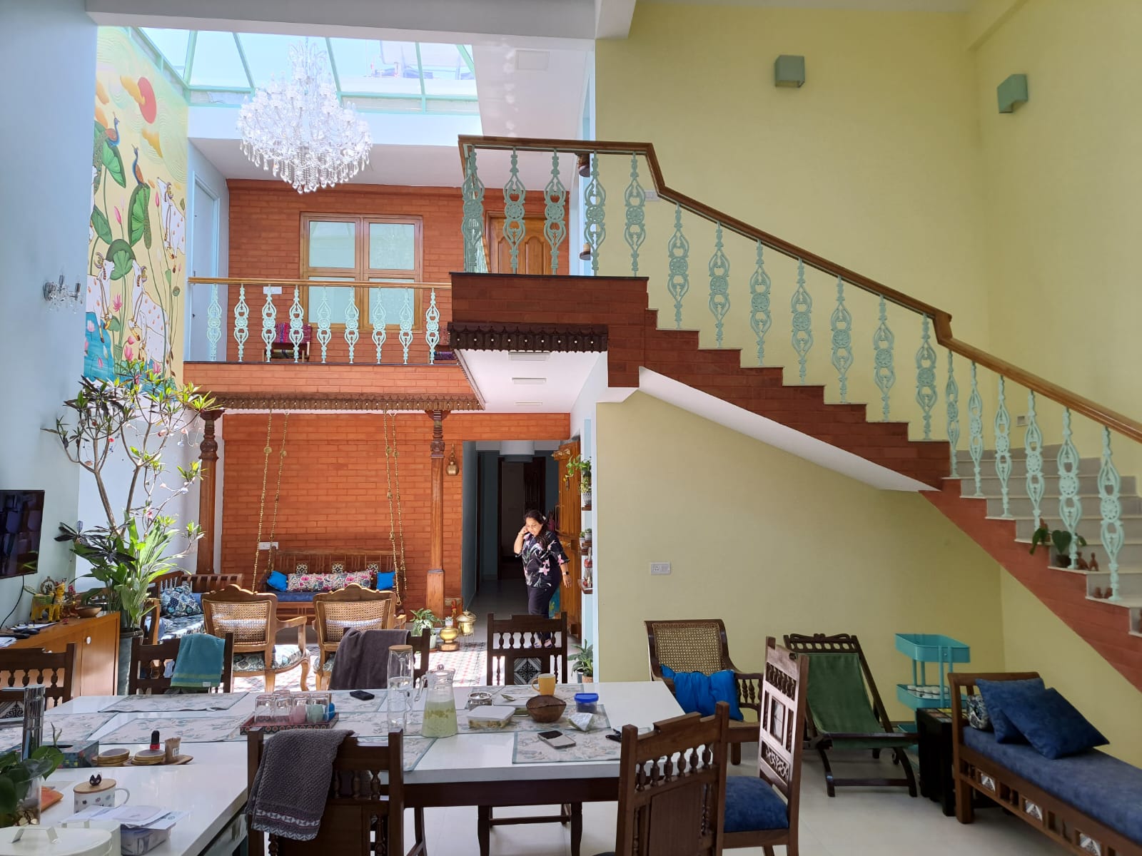 Double-height atrium dining and lounge space with a wrought-iron staircase, a brick-clad mezzanine with a traditional swing