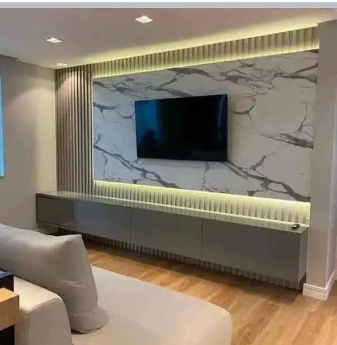 Wide living-room TV wall in grey-veined marble framed above and below by backlit fluted bands