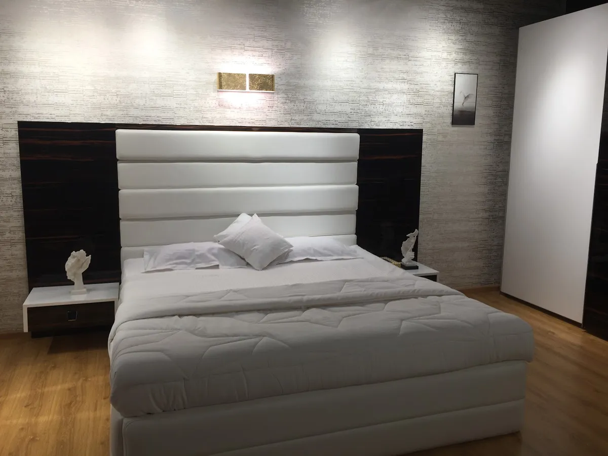 Bedroom with a tall white channel-upholstered headboard set against high-gloss dark macassar wall panels