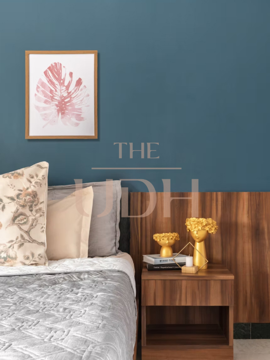 Bedroom corner with a deep teal accent wall, a wood-panel headboard, and a walnut nightstand styled with gold decor and a framed leaf print.