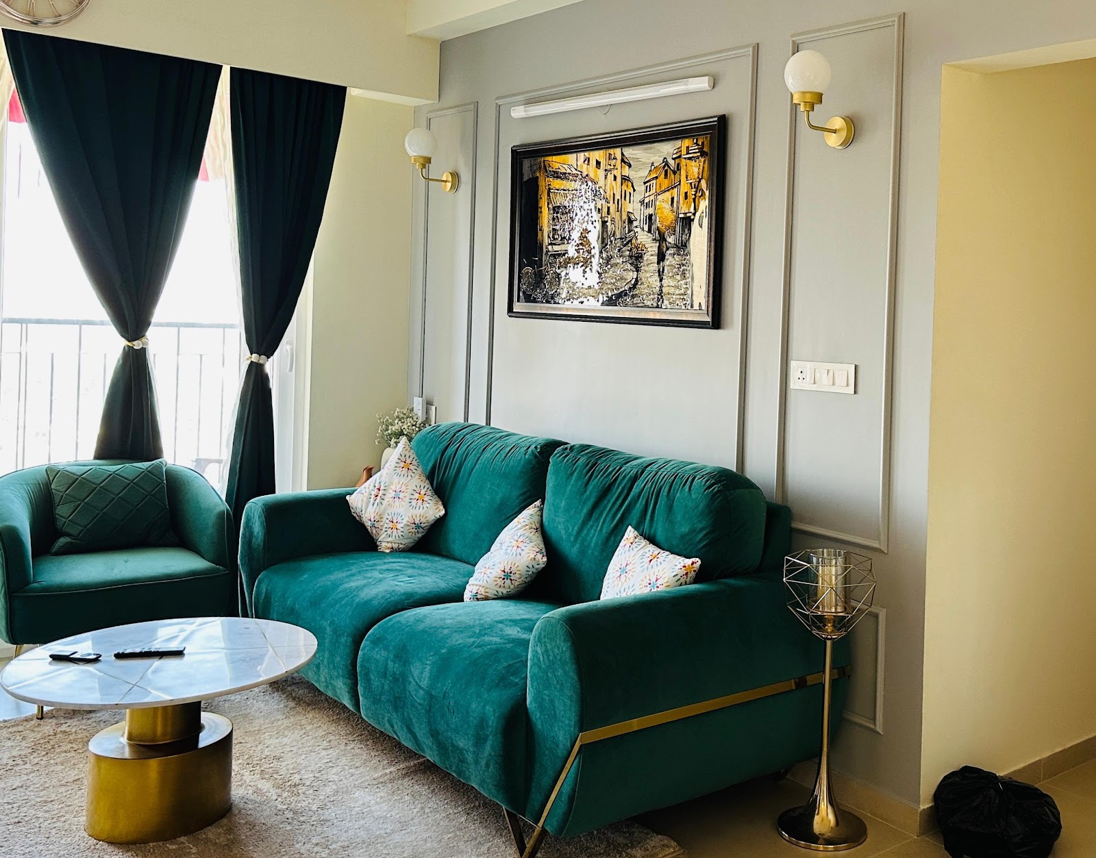 Living room with an emerald velvet sofa and armchair trimmed in brass, a round white marble coffee table on a brass base, wall panel moulding
