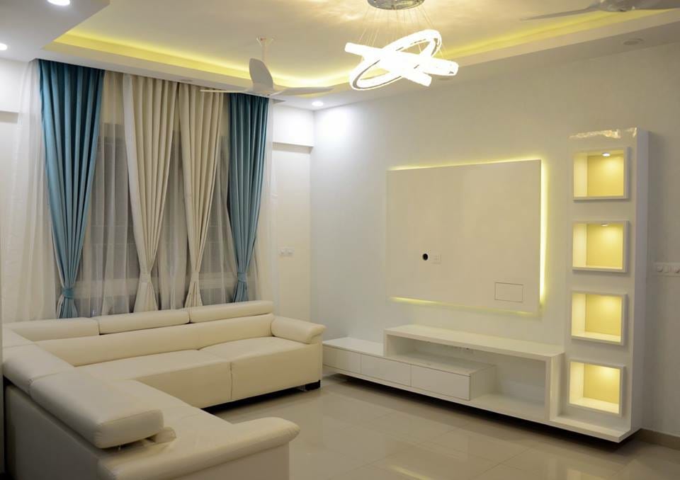 Living room with a white L-shaped sofa, teal-and-cream layered curtains and a backlit TV wall unit with glowing display niches.
