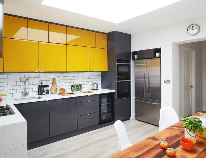 L-shaped kitchen with high-gloss yellow upper cabinets over charcoal lower units, white subway-tile splashback and an integrated stainless steel fridge-freezer