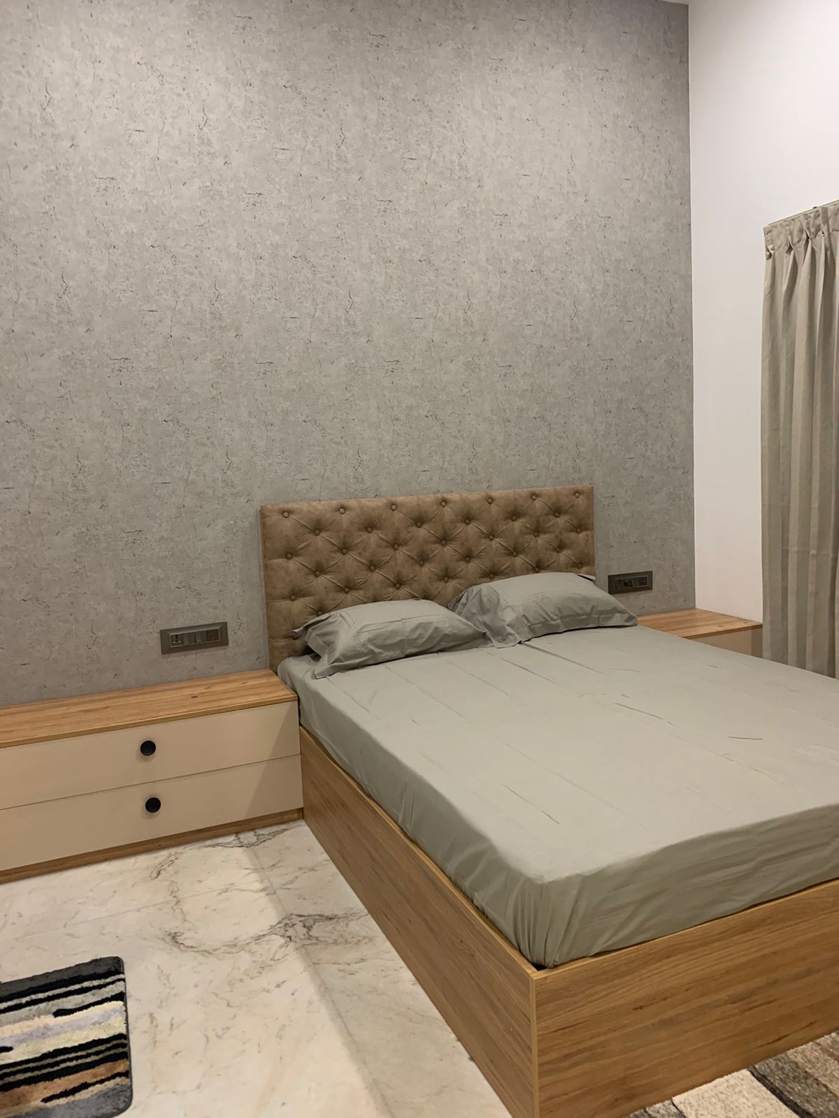 Bedroom with a grey textured-wallpaper headboard wall, a tufted tan upholstered headboard, a wood storage-bed platform